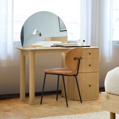 a desk with a mirror and chair next to it in front of a window on a wooden floor