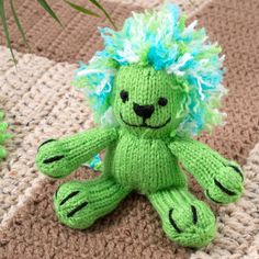 a small green stuffed animal sitting on top of a rug next to a plant in a pot