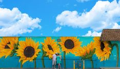 two people standing in front of a painted wall with sunflowers