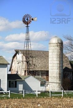 an old farm with a windmill and two barns in the foreground, on a sunny day