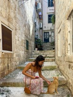 a woman kneeling down petting a cat in an alleyway next to stone steps