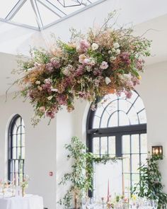 an arrangement of flowers is suspended from the ceiling over a dining room table with white linens