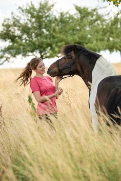 a woman standing next to a brown and white horse on top of a dry grass field