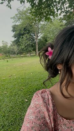 a woman with a flower in her hair is sitting on the grass and looking into the distance