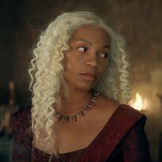 a woman with long white hair in a red dress looking at the camera while wearing a necklace