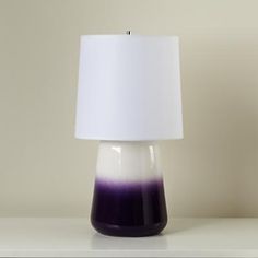 a purple and white lamp sitting on top of a table next to a black vase