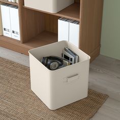 a white storage box sitting on top of a rug next to a bookshelf