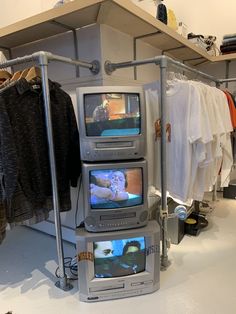 two televisions sitting on top of each other in a room with clothes hanging up