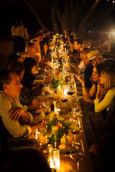 a group of people sitting at a long table with candles in front of their faces