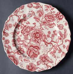 an old red and white plate with flowers on the front, sitting on a gray surface