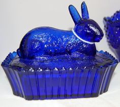 a blue glass rabbit sitting on top of a muffin shaped bowl with its mouth open