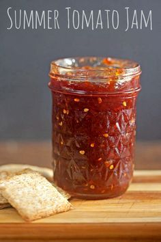 a jar filled with tomato jam next to crackers on a cutting board and the words summer tomato jam