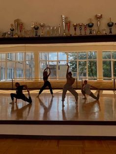 four people doing yoga poses in front of trophies on the wall and windows behind them