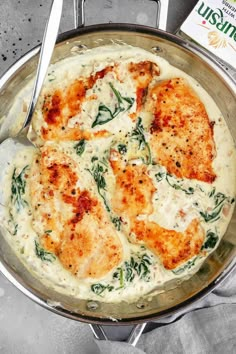 a pan filled with chicken and spinach on top of a table next to a book