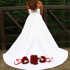 a woman in a white wedding dress standing on a bridge with red roses around her