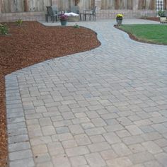 a brick walkway in front of a wooden fence with chairs and table on it,