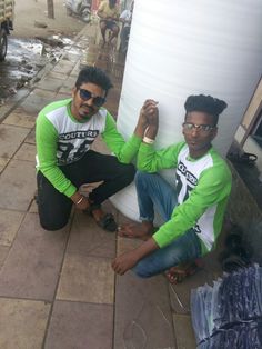 two young men sitting on the ground next to a large white tank and one is wearing sunglasses