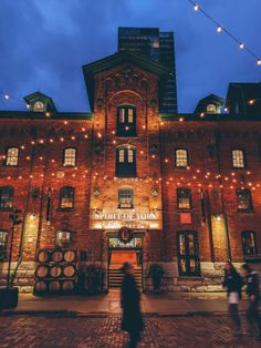 people are walking in front of an old brick building with lights on the sides and windows