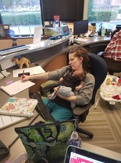 a woman holding a baby in her lap while sitting at a desk with other office supplies