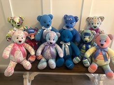 a group of teddy bears sitting on top of a wooden bench next to each other