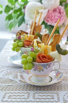 a cup filled with fruit and veggies on top of a table next to flowers