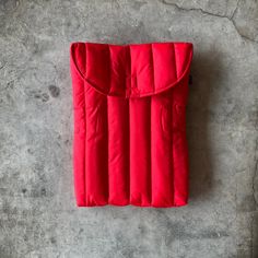 a red sleeping bag laying on top of a cement floor next to a white wall