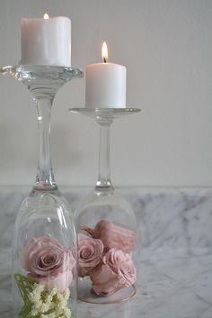 two glass vases with flowers in them on a marble counter top next to candles