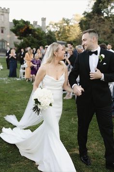 a bride and groom walking through the grass at their outdoor wedding in front of an audience