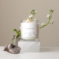 a white candle sitting on top of a table next to rocks and a vase with flowers