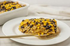 a white plate topped with food next to a casserole covered in beans and corn