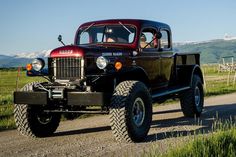 an old red truck driving down a dirt road