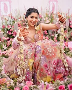 a woman sitting on top of a lush green field covered in pink and yellow flowers