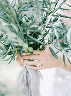 a close up of a person's hands holding a bouquet of flowers and greenery