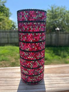 a vase made out of beads sitting on top of a wooden table next to a fence