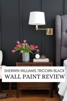 a bedroom with black walls and pink flowers in a vase on the end table next to a gray headboard