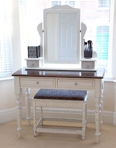 a white dressing table with a mirror and stool in front of the window next to it