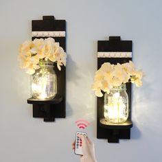 two mason jars with flowers in them are on the wall next to a remote control