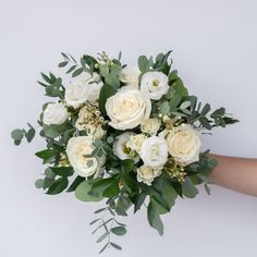 a bouquet of white roses and greenery is held by someone's hand on a white background