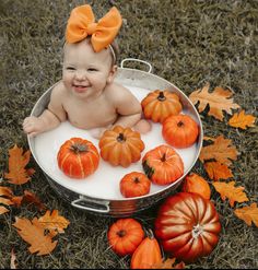 a baby sitting in a tub with pumpkins and leaves around it on the ground