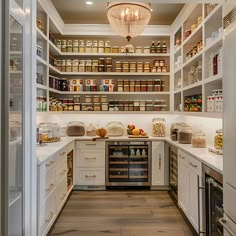 Explore this luxurious walk-in kitchen pantry featuring white cabinets and open shelving stacked with neatly organized food items. Gleaming white marble countertops and modern stainless steel appliances add a touch of sophistication. Highlighted by a brass pendant chandelier and natural wood floors, the space includes a wine cooler and a dual-door fridge, perfectly blending functionality with farmhouse elegance. Pantry With Chandelier, Big Modern Pantry, Organized Food Cabinet, Farmhouse Storage Room, House Design Pantry, Huge Storage Room, Dream Walk In Pantry, Butlers Pantry With Appliances, Walk In Pantry With Appliances