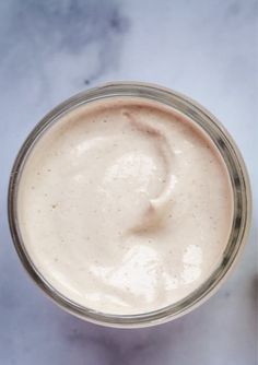 a glass jar filled with cream sitting on top of a marble counter next to a spoon