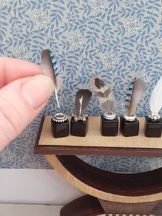 a person holding a small wooden stand with four miniature items on it and a feather quill in the middle