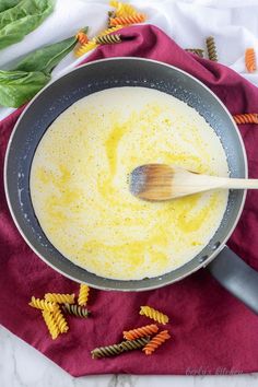 a pan filled with yellow sauce on top of a red towel next to pasta noodles