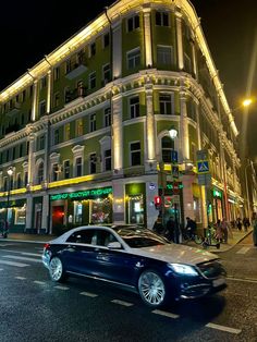 a car is driving down the street in front of a large building at night time