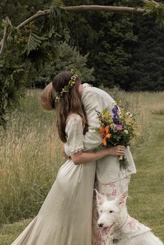 two women in wedding gowns hugging each other with a white dog standing next to them