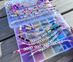 two plastic trays filled with beads and bracelets on top of a wooden table