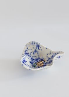 a blue and white porcelain bird dish on a white surface with a gold ring in it's mouth