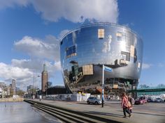 two people walking on the sidewalk in front of a large building with a mirrored facade