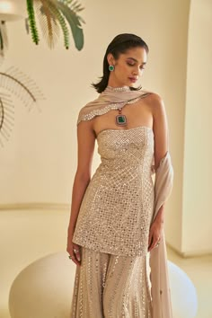 This nude georgette sharara set features all-over mirror work and is paired with a four-sided embroidered dupatta. The peplum top comes with optional straps.From Seema Gujral's Fiori collection. DELIVERY TIMEPlease allow 8-12 weeks for your outfit to arrive. FABRIC DETAILSGeorgette Professional cleaning only. Peplum Top Sharara Designs, Mirror Work Indian Outfit, Wedding Outfit Inspo Indian, Strapless Indian Outfit, Goa Wedding Outfits, Seema Gujral Lehenga, Sharara Outfits Indian, Sister Wedding Outfit, Desi Fusion Outfits