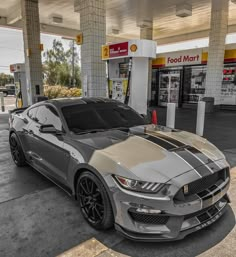 a silver and black mustang parked in front of a gas station with no one around